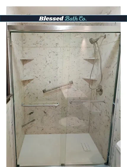 Walk-in shower with a sliding glass door, corner shelves and grab bars on marble-look walls