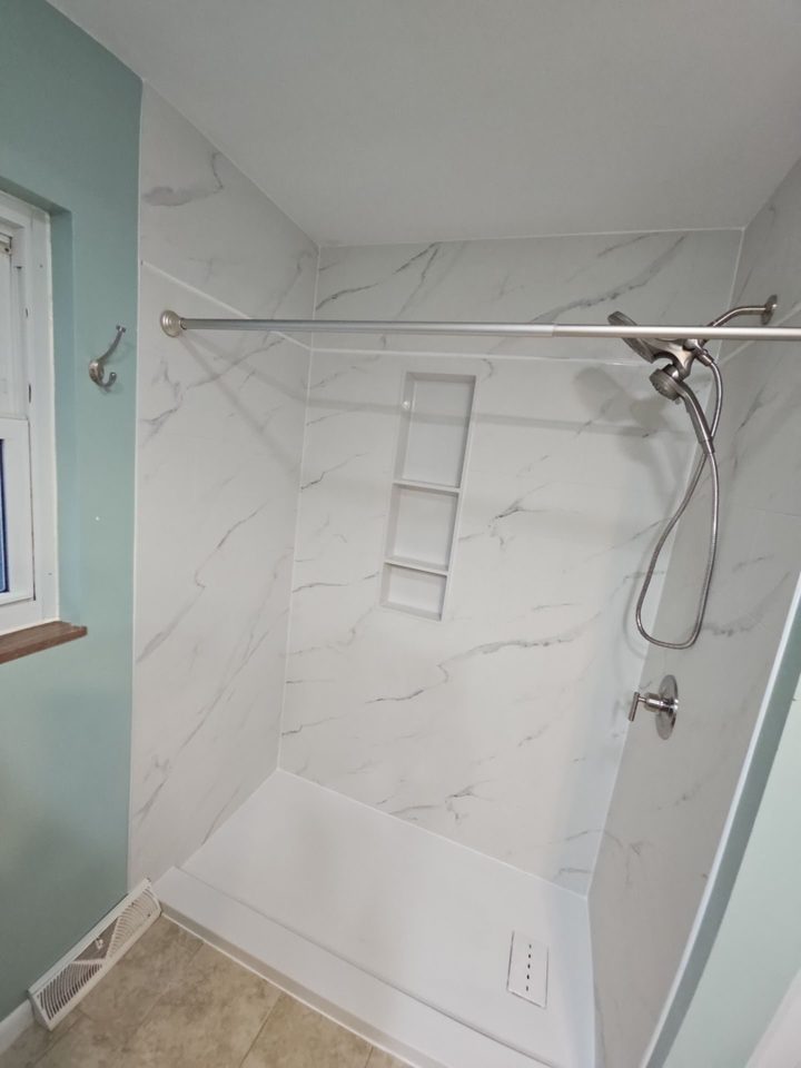 After: a walk-in shower with marble-look walls and a white shower pan