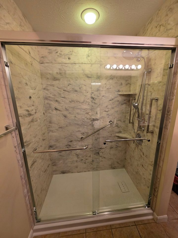 After: a walk-in shower with a sliding glass door, dark marble-look tile and grab bars